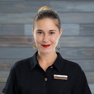 A portrait of Moira Masshardt. She is a white woman with her hair in a bun and a black polo.