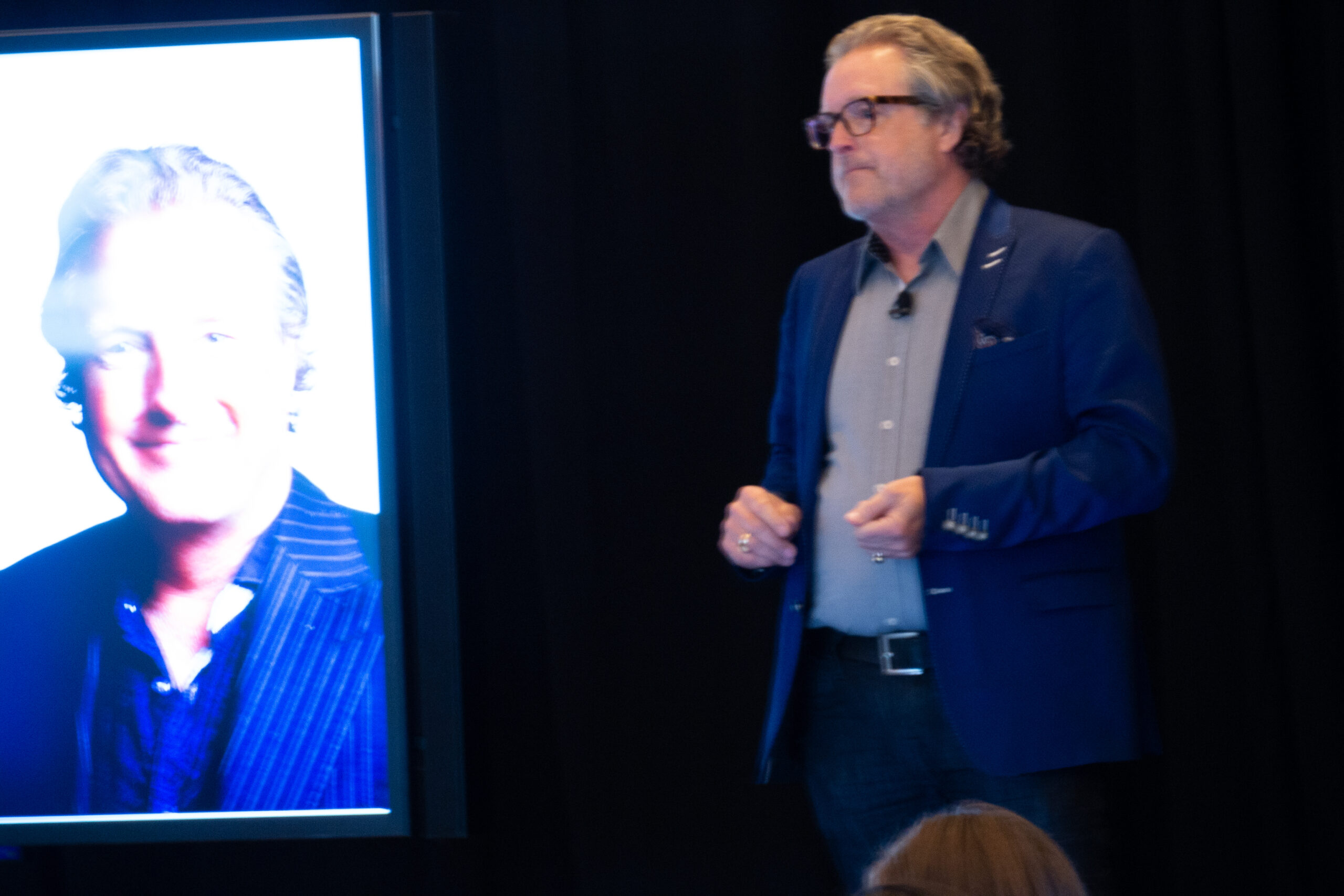 Author Daren Martin, PhD, speaks onstage. He has a stubbled gray beard and a blue suit jacket.