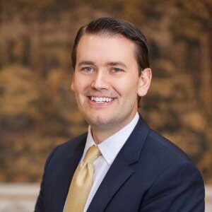 A portrait of Peter Andersen. He is a white man with short hair, a dark suit and a yellow tie.