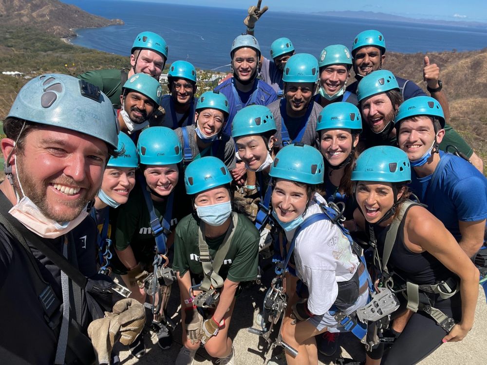 A group of coworkers on a teambuilding excursion. They are wearing blue helmets and ziplining harnesses.
