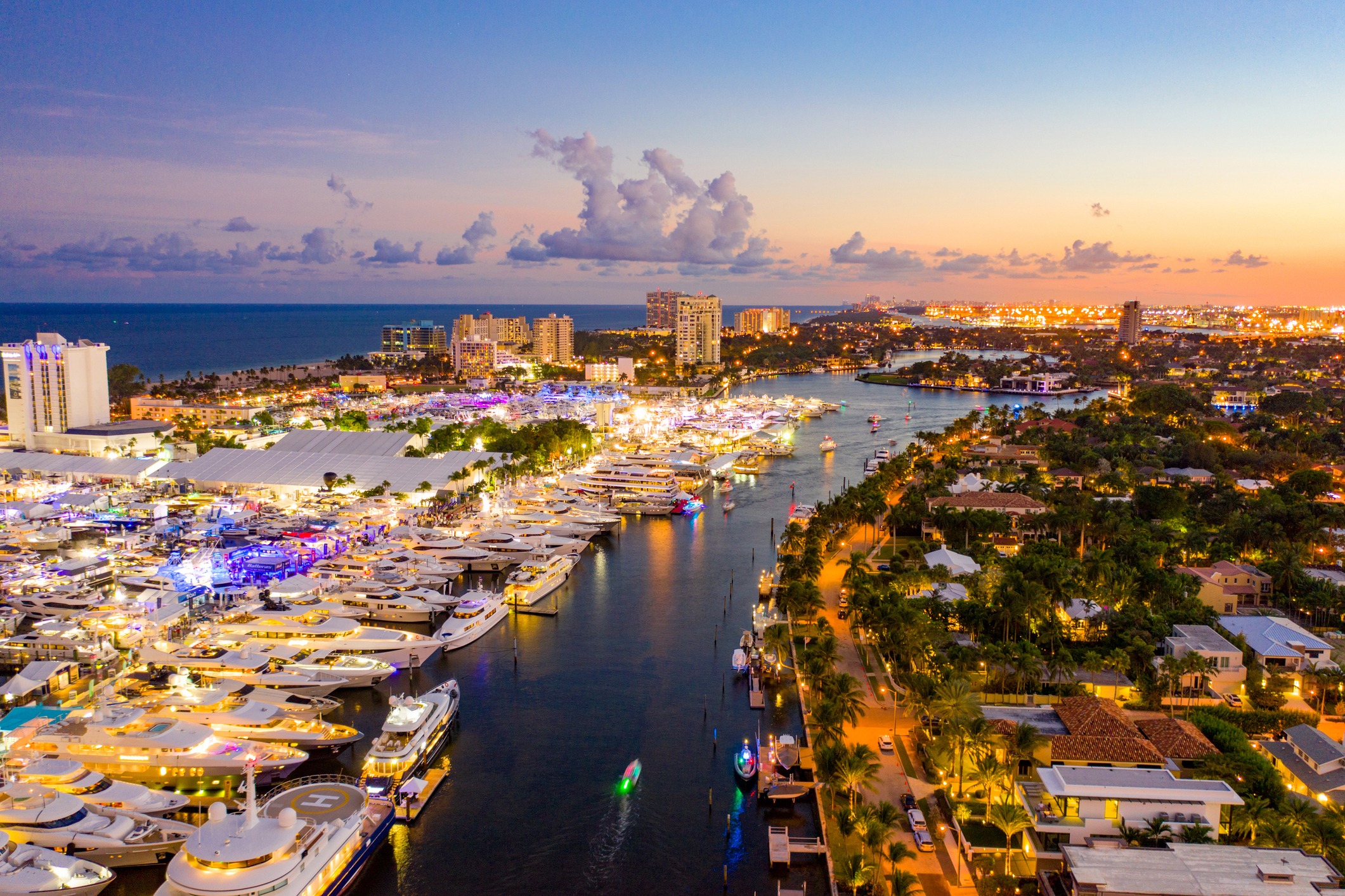 An overhead shot of Ford Lauderdale, Florida at dusk. Yachts are docked along a canal across from homes and palm trees.
