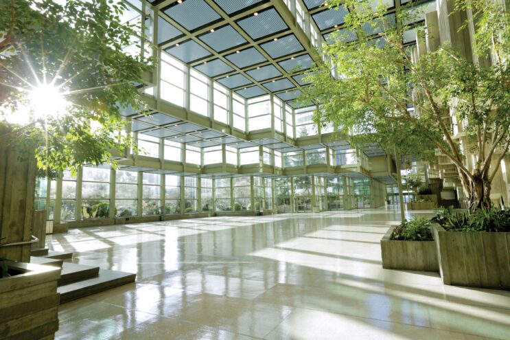 The atrium of the Seattle Convention Center. The walls and ceiling are glass, large potted plants are on the sides of the room.