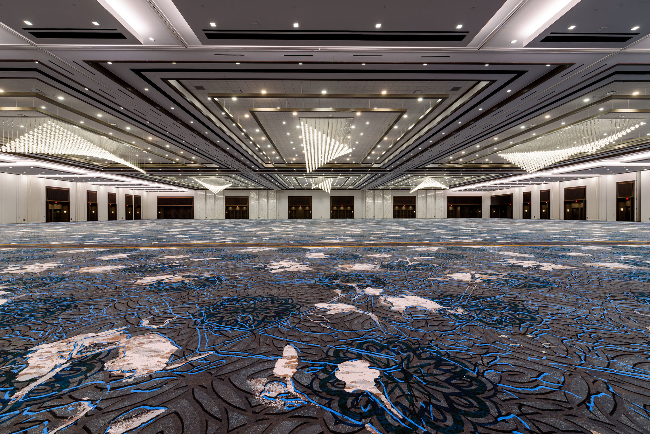 A ballroom at Caesars Forum in Las Vegas. The carpet is an abstract granite-like pattern with blue highlights. The ceiling is intricately inlaid with dotted lights.