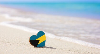 Flag of the Bahamas in the shape of a heart on a sandy beach.