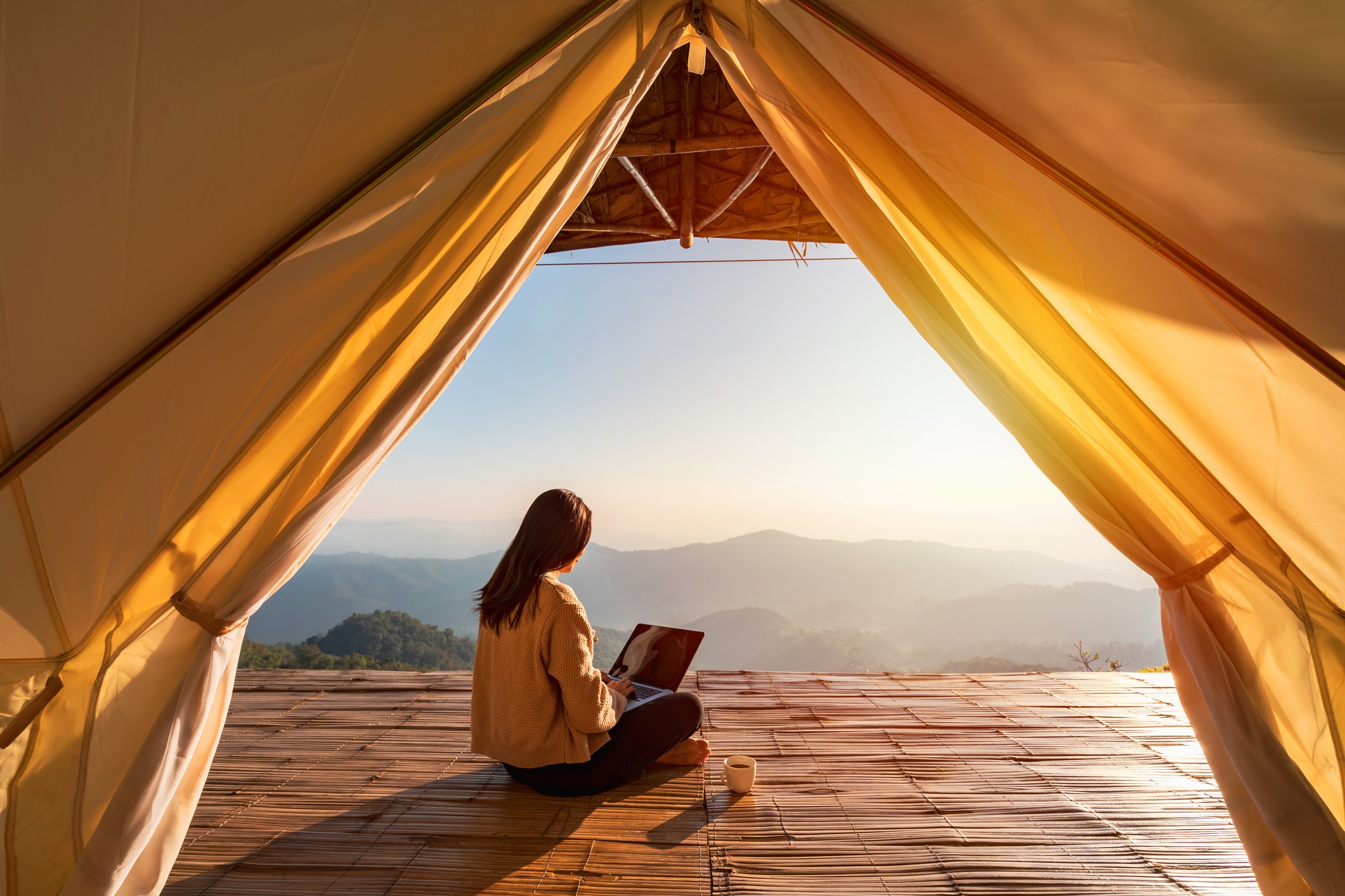 A woman on her laptop sits in front of a distant mountain range.