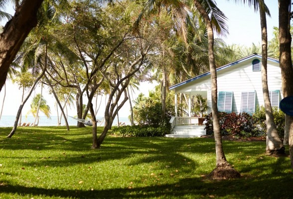 The Moorings Village. A white beach house is on a lawn surrounded by trees. The ocean is visible behind.