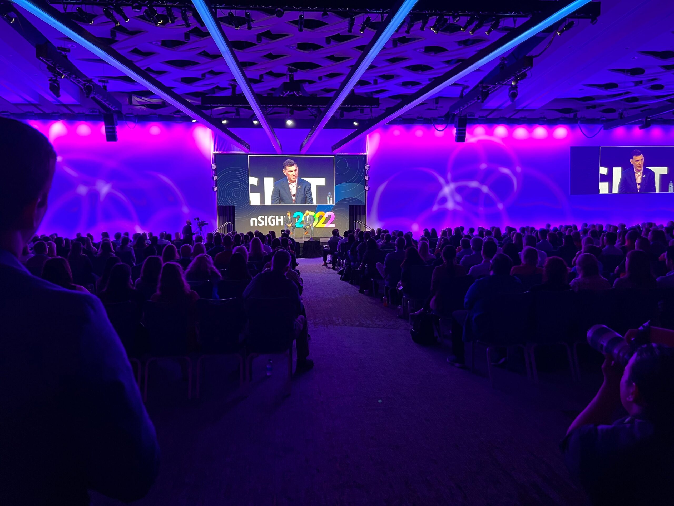 A crowd watches a speaker during nSight 2022. There are purple lights on either side of the projector.