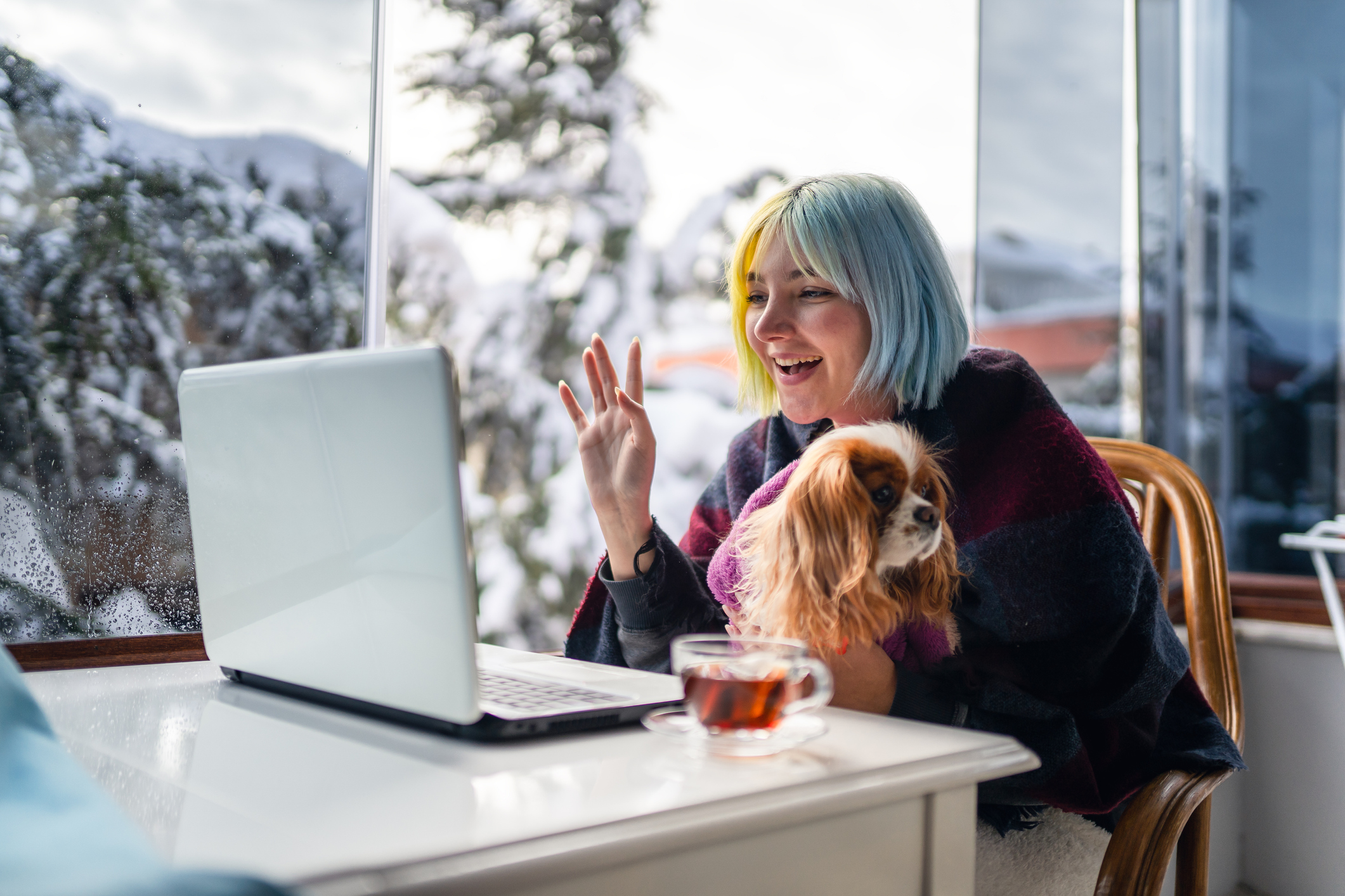 Woman sitting at desk with laptop, cuddling with dog in lap. 