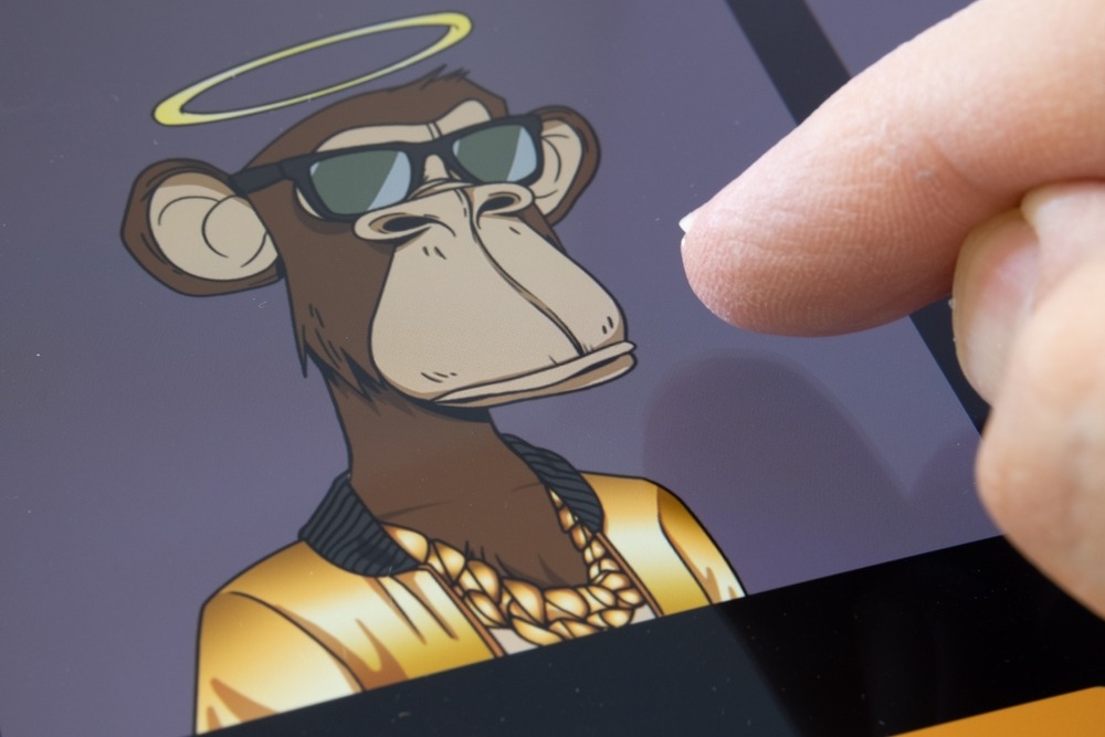 person using ipad that has a "bored ape" nft image of ape with halo wearing gold chain, gold jacket black glasses on its screen