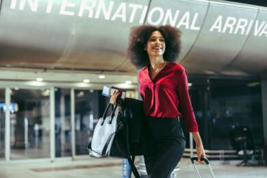 smiling woman with luggage walking at international airport