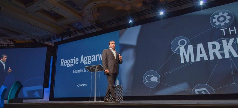 Photo of Reggie Aggarwal walking across blue stage at Cvent Connect