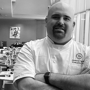 black and white photo of Chef Andrew Cardi crossing arms and wearing white dress shirt