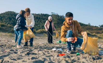 Young man picking up trash with group of volunteers on the beach