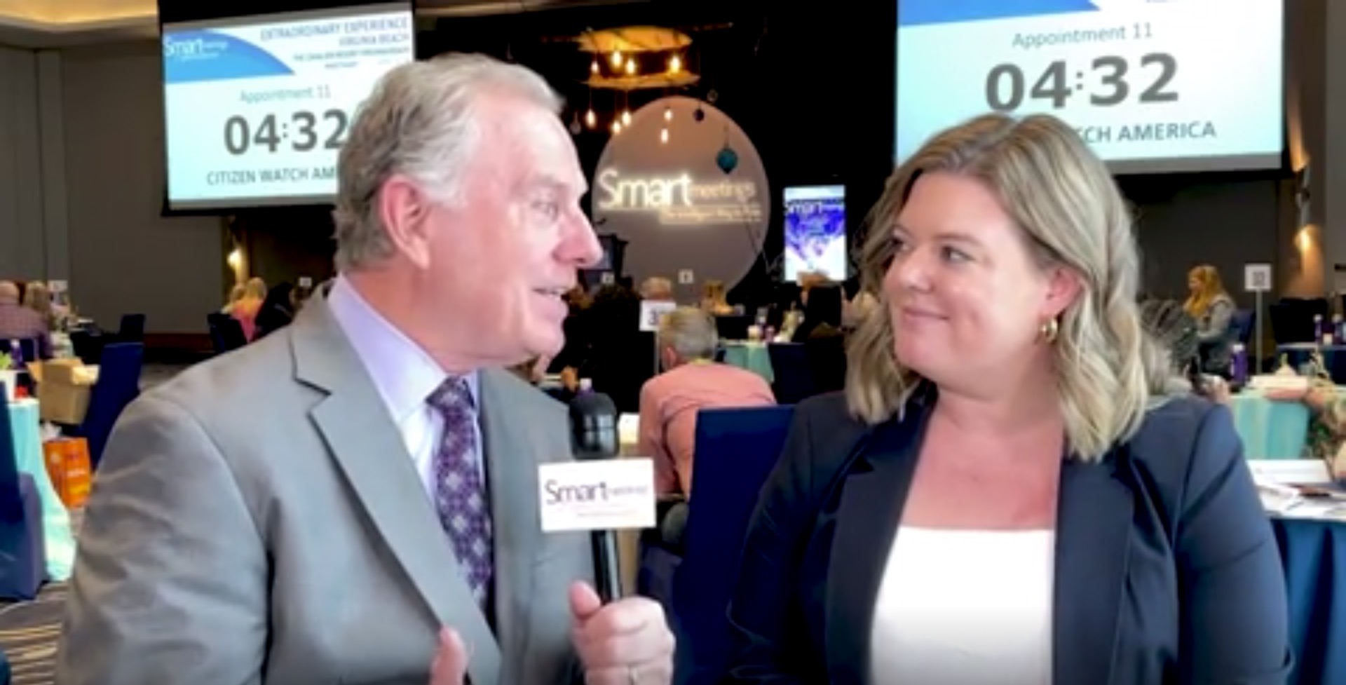 mike lyons wearing grey suit talking to woman wearing white dress shirt and black coat