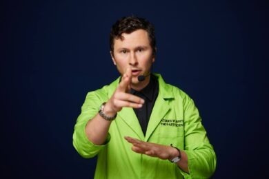man wearing neon green lab coat and pointing at camera