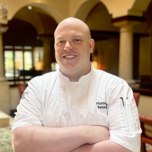 A man in a chef's uniform smiles into the camera