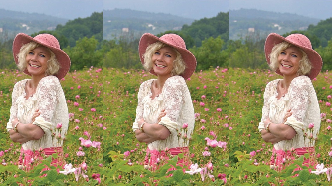 woman smiling, standing among pink flowers