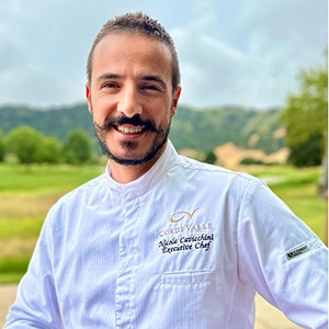 A man in a chef uniform smiles into the camera