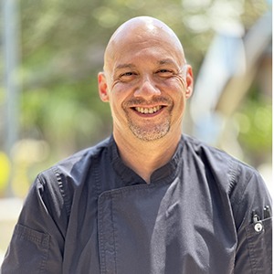 A man in a chef uniform smiles into the camera