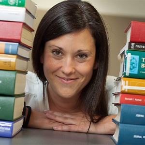 woman smiling, resting hands on table among books